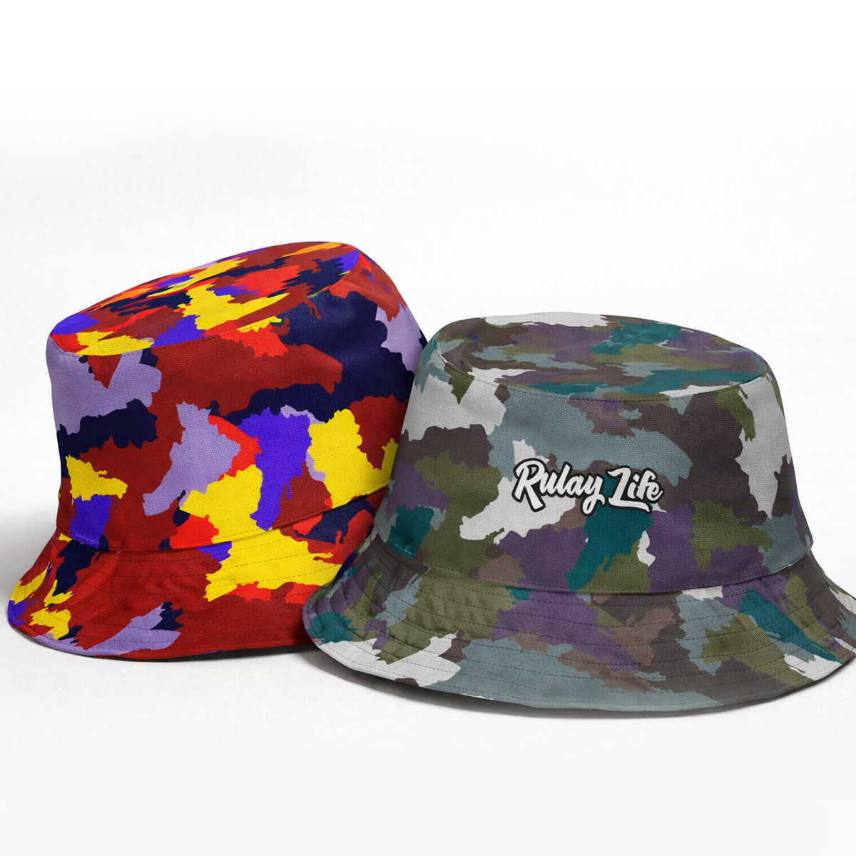 Two bucket hats, one multicolored and one with 'Rulay Life' logo, on a white background. Dominican Camo Reversible bucket hat (Ember Dawn/Midnight Desert)