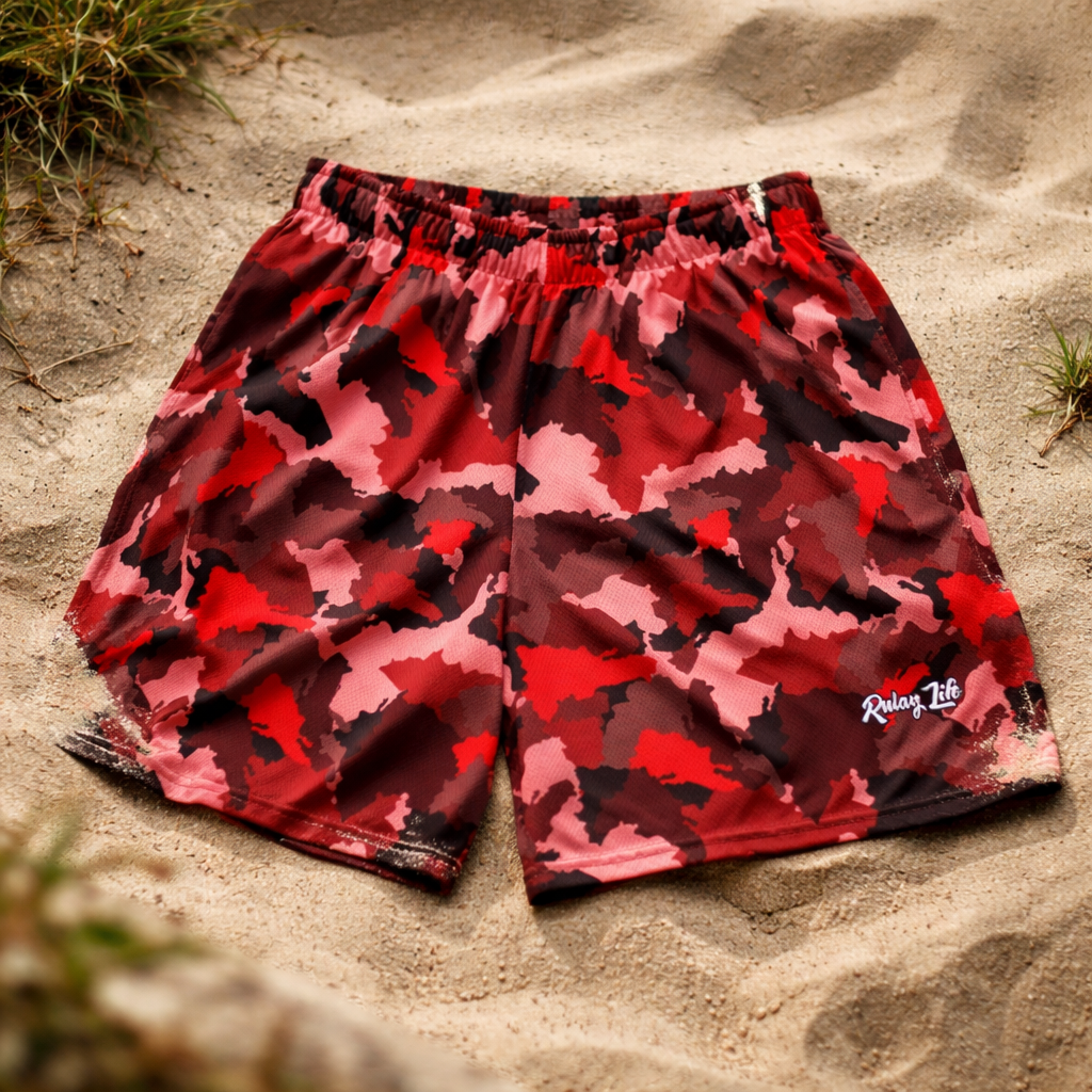 Red and black camouflage shorts on a sandy surface. Ruby Dominican shorts